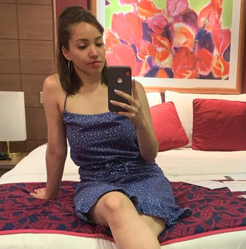 Erica photographing herself in a mirror, sitting on a bed
