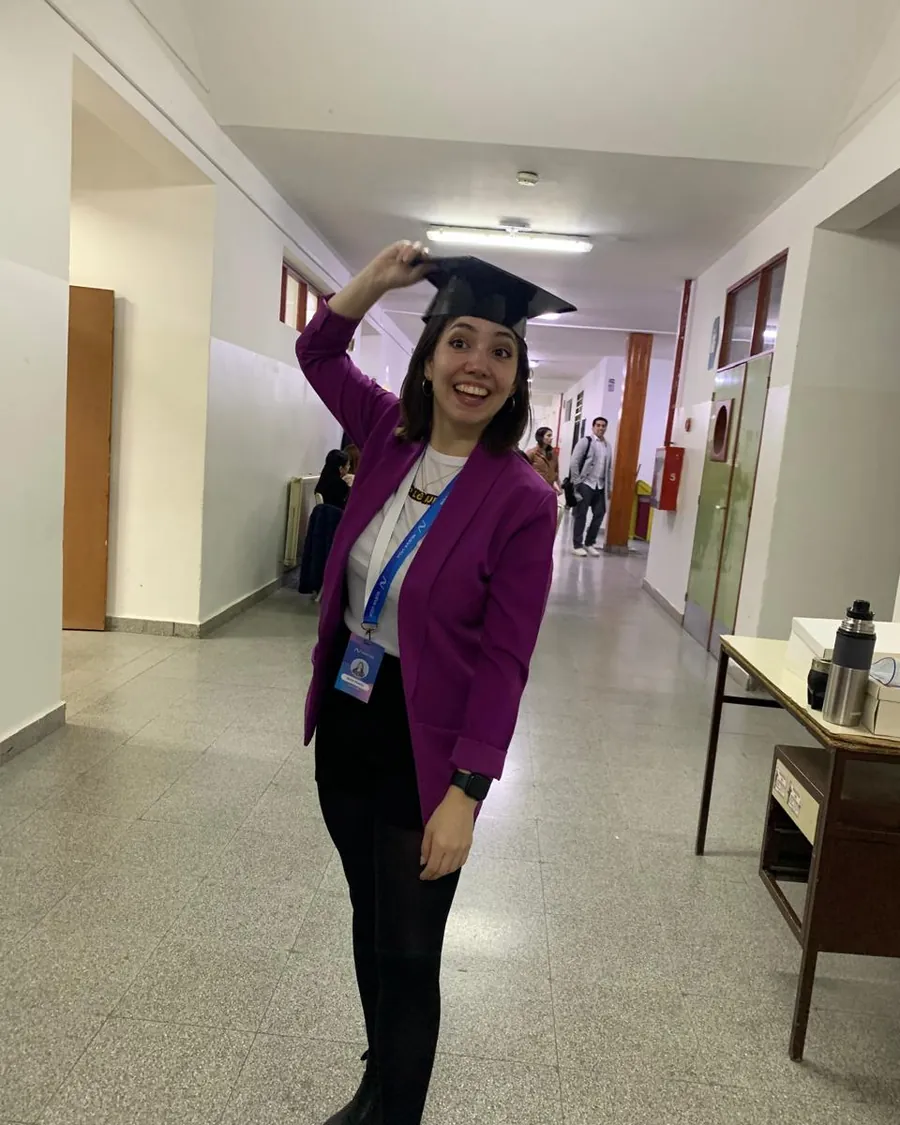 Erica in the school corridor in a violet blazer, lifting her graduation cap off her head