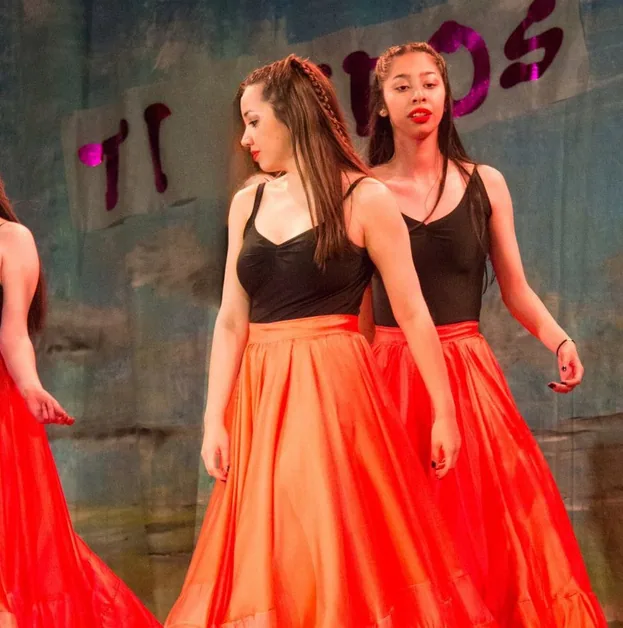 Erica dancing with a partner, both in long orange skirts, mid-step
