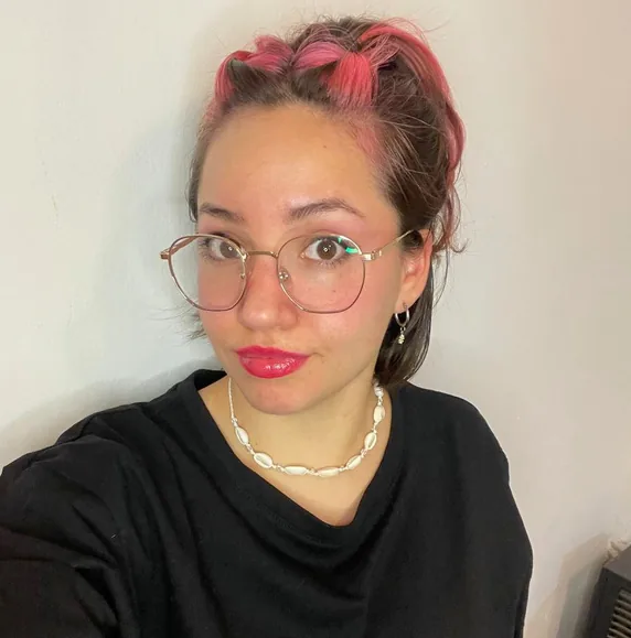 Erica in a black tee, hair braided through with pink, looking straight at the camera