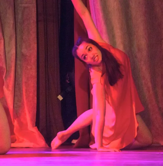Erica low on the stage floor in red light, one arm swept overhead